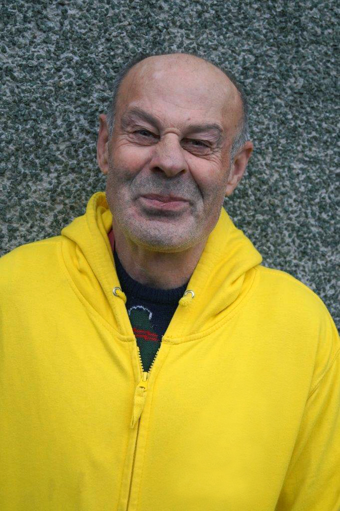 A man in his 50s wearing a bright yellow hoody smiles for the camera