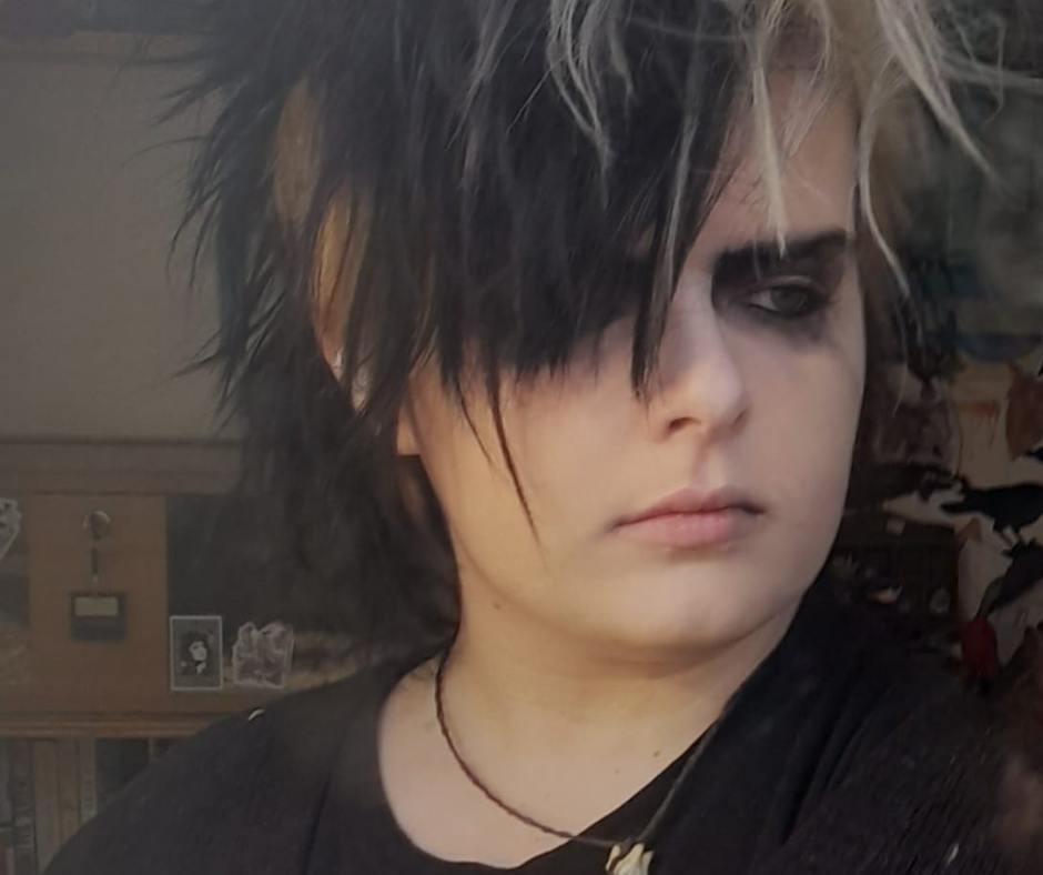A young person with back-combed black and white hair, pale skin and heavy black eye makeup