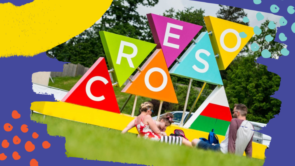 An installation on the Urdd Esiteddfod maes spells out Croeso in colourful triangles, young people relax on the grass in front of the sign